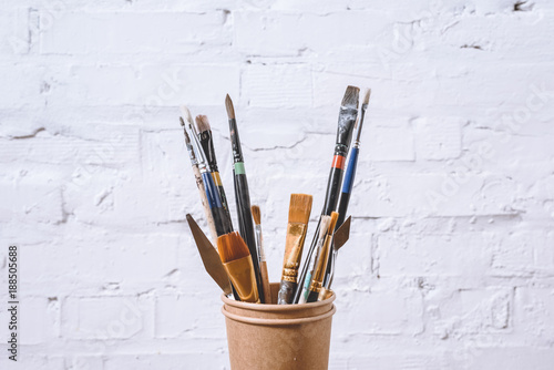 paint brushes in paper cups on white wall