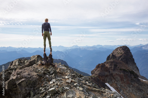 Adventurous people are performing a stunt on top of a rocky mountain. Taken on top of Skypilot Peak  Near Squamish  North of Vancouver  British Columbia  Canada.
