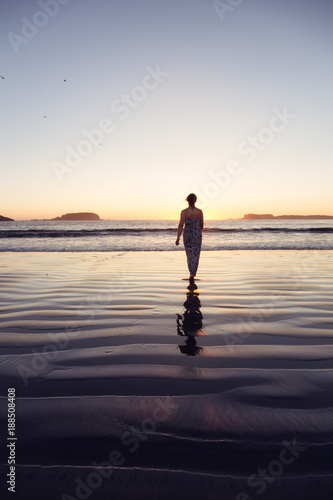 Woman Walking on a Sandy Beach during a vibrant and colorful summer sunset. Taken in Tofino, Vancouver Island, BC, Canada.