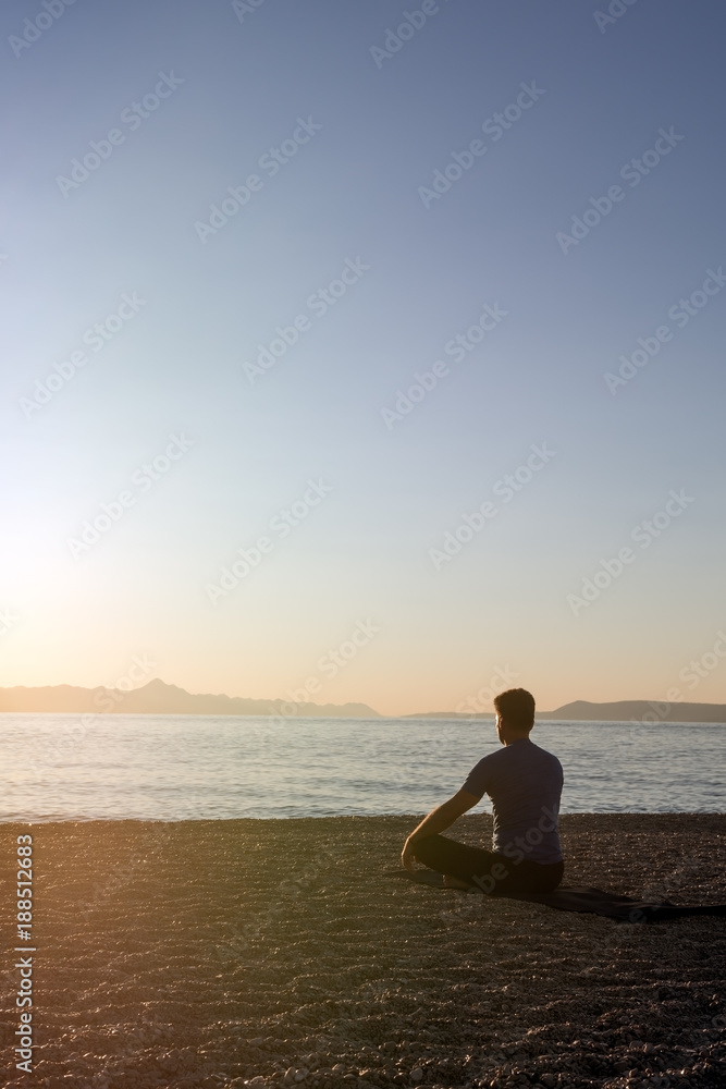 An adult male meditating on the beach at the seashore in the morning