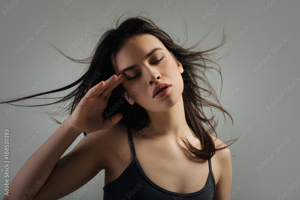 Closing eyes. Attractive unsmiling dark-haired young woman thinking and having her eyes closed and touching her temple Closing eyes. Attractive unsmiling dark-haired young woman thinking and having her eyes closed and touching her temple