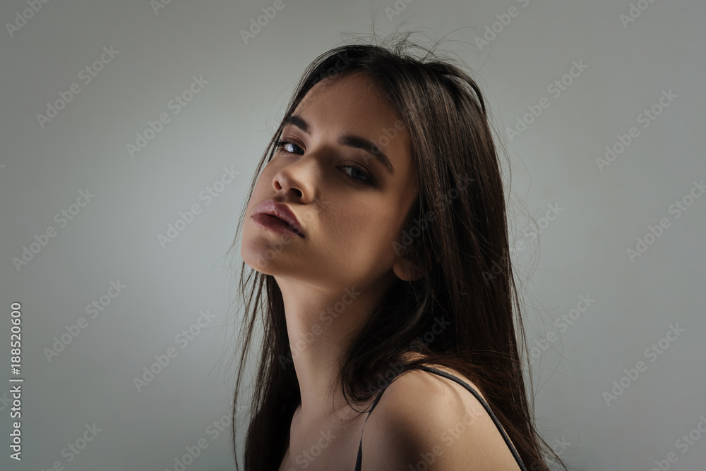 Serious. Attractive unsmiling dark-haired young woman looking over her shoulder and thinking and wearing a top Serious. Attractive unsmiling dark-haired young woman looking over her shoulder and thinking and wearing a top