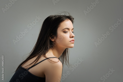 Preoccupied. Beautiful serious long-haired young woman thinking and looking in the distance and wearing a top