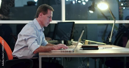 Manager in white shirt sitting at the table in office. Working on laptop. Late work overtime concept.