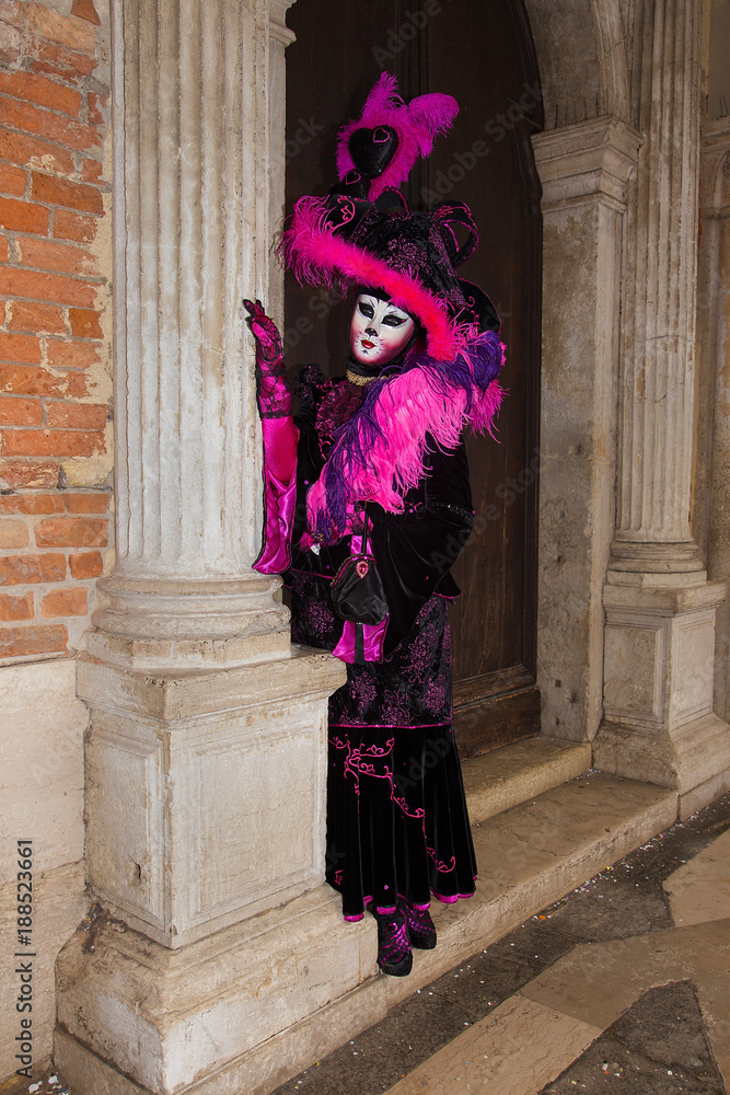 Female Venetian Mask - Cat mask in pink / black elegant costume on St. Mark's Square in Venice with traditional venetian pillar - Venice Carnival Female Venetian Mask - Cat mask in pink / black elegant costume on St. Mark's Square in Venice with traditional venetian pillar - Venice Carnival