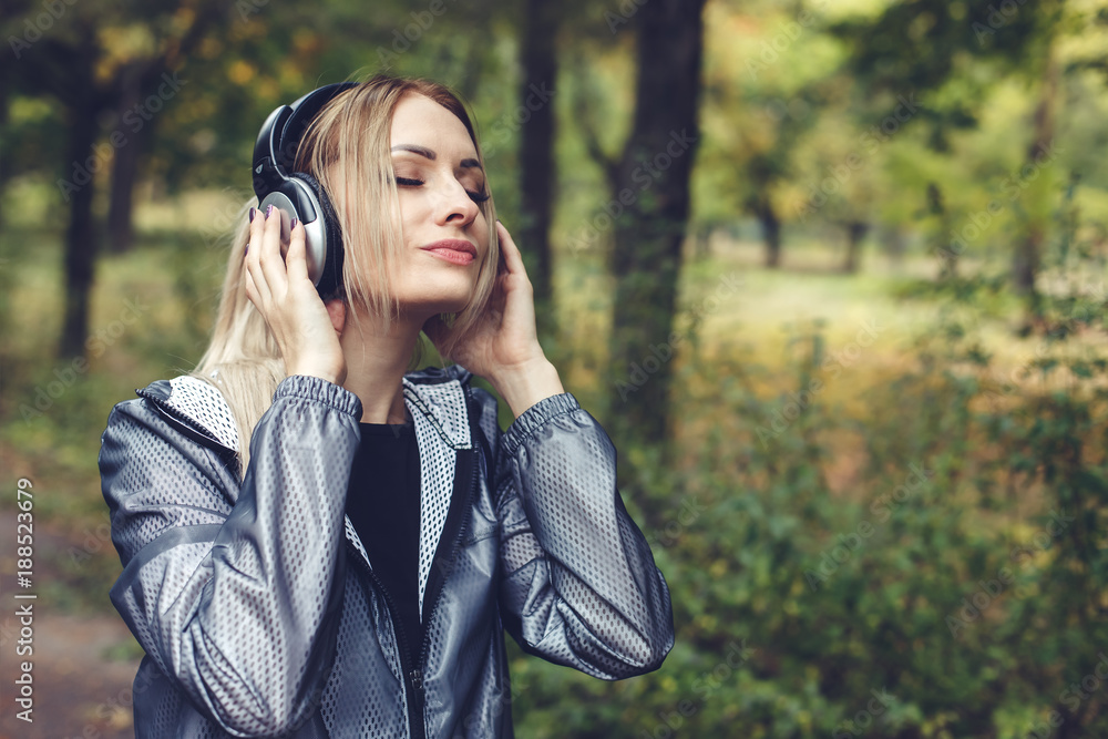 beautiful young woman walking on a park,  listening to music on headphones.