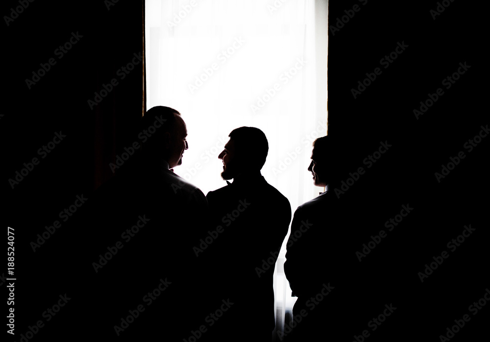 Silhouettes of three man standing before a bright window