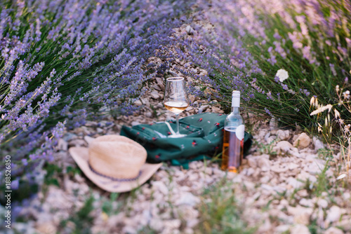 Fototapeta Naklejka Na Ścianę i Meble -  Picnic outdoors in lavender fields in Provence, south France. Rose wine in a glass, whole bottle of wine and a travel backpack  