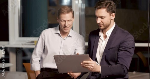 Two partners are looking at the tablet screen and discuss data of new project. Late work overtime concept.