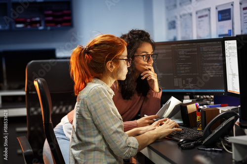 Late at night, two dedicated female programmers work side by side, driven to meet project deadlines, fueled by determination, and sustained by coffee, as they strive for innovation together. photo