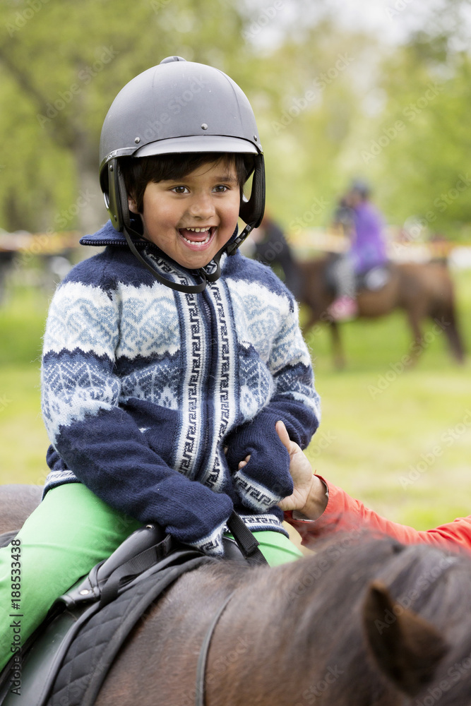 Excited little boy in helmet riding horse Excited little boy in helmet riding horseÂ
