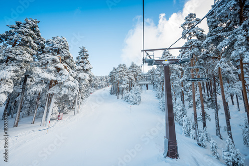 A winter view of a ski resort full of fresh snow taken from the chairlift going through a forest, in Madrid, Spain