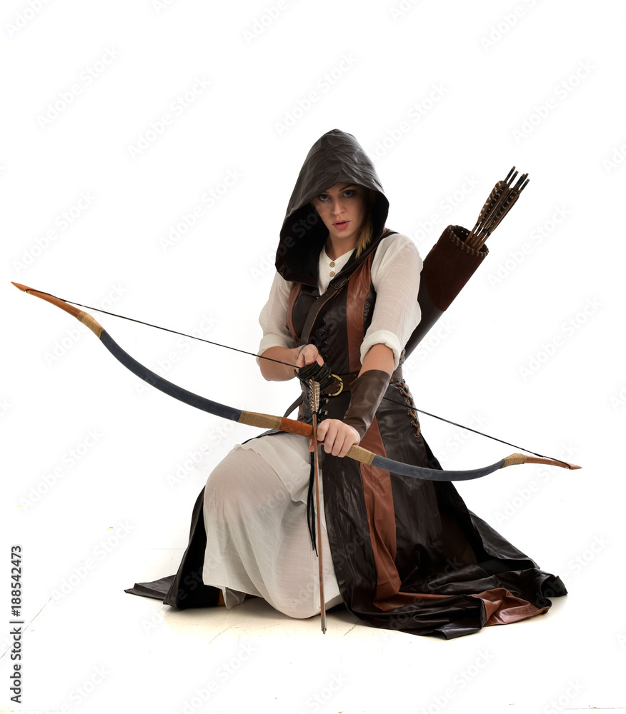 Obraz premium full length portrait of girl wearing brown fantasy costume, holding a bow and arrow, on white studio background. 
