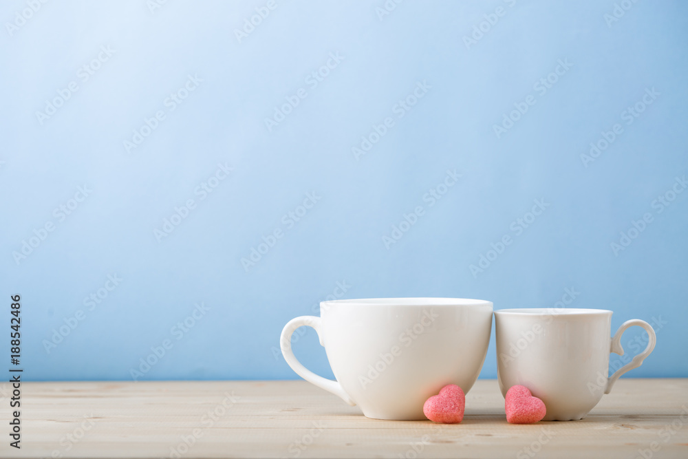 Valentines day concept, mugs cups of coffee or tea for two lovers honeymoon wedding morning surprise breakfast, pink heart sugar candies, blue background pastel colors copy space, light wooden table Valentines day concept, mugs cups of coffee or tea for two lovers honeymoon wedding morning surprise breakfast, pink heart sugar candies, blue background pastel colors copy space, light wooden table