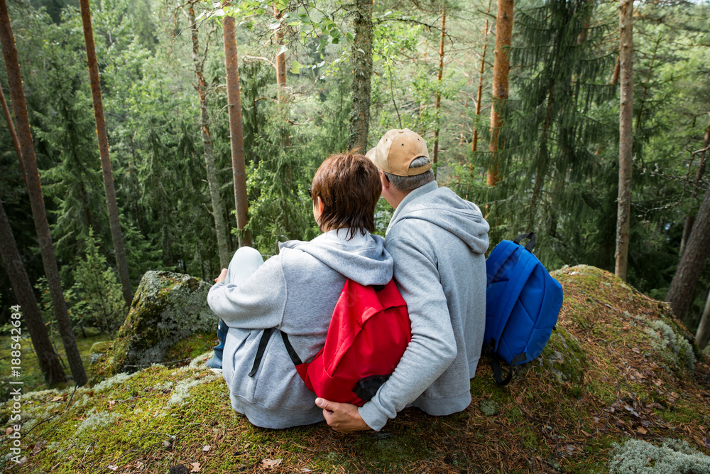 Loving senior couple hiking, sitting on the top of rock in forest, exploring. Active Mature man and woman hugging and Happily smiling. Scenic view. Healthy lifestyle. Finland. Loving senior couple hiking, sitting on the top of rock in forest, exploring. Active Mature man and woman hugging and Happily smiling. Scenic view. Healthy lifestyle. Finland.