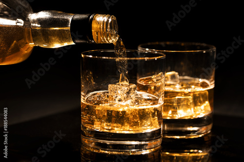 pouring whiskey into a glass with ice cubes on black background