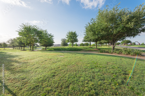 Panorama view of urban park near residential area neighborhood in Sugarland, Texas, US. Beautiful green grass lawn, oak trees and walking/biking path illuminate by sunshine during early spring morning photo