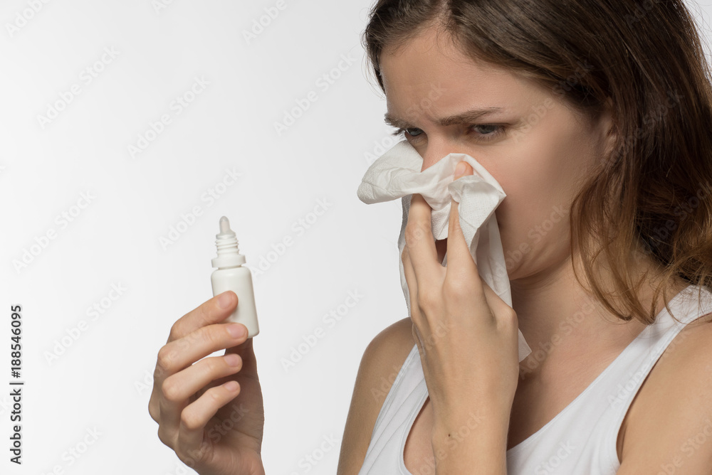 A beautiful brunette woman gets sick and a runny nose, digs her nose with medicine and holds a white paper kerchief A beautiful brunette woman gets sick and a runny nose, digs her nose with medicine and holds a white paper kerchief