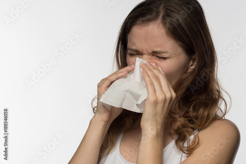 A beautiful brunette woman becomes ill with a cold and runny nose, sneezes and coughs into a white paper kerchief