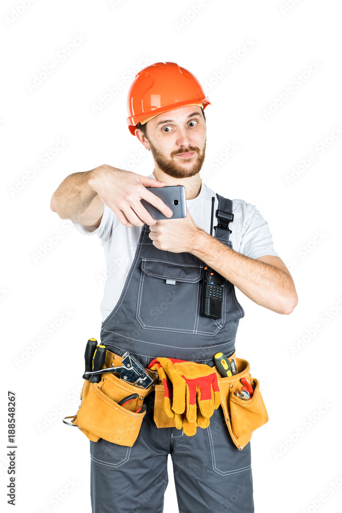 Smiling young construction worker showing a sign and taking a picture from the phone. Repair and construction. Isolated on white background Smiling young construction worker showing a sign and taking a picture from the phone. Repair and construction. Isolated on white background