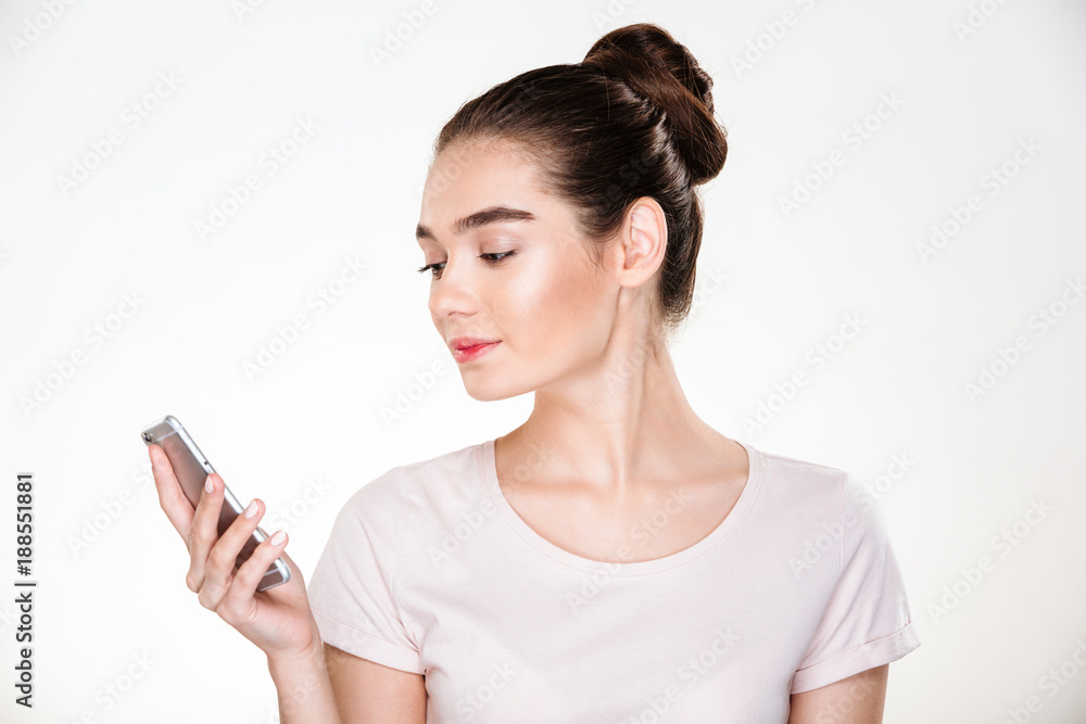 Picture of female with brown hair in bun chatting or reading ebook using smartphone isolated over white background Picture of female with brown hair in bun chatting or reading ebook using smartphone isolated over white background
