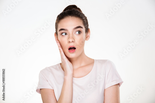 Pretty woman with brown hair in bun touching her face expressing surprise or shock posing isolated over white background