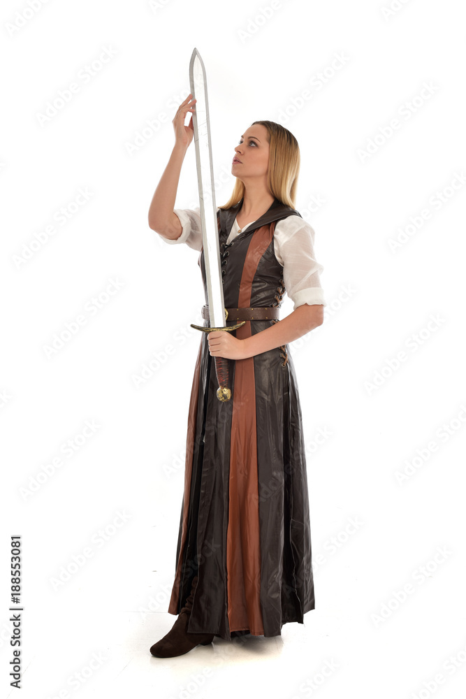 full length portrait of girl wearing brown fantasy costume, holding a sword. standing pose on white studio background. full length portrait of girl wearing brown fantasy costume, holding a sword. standing pose on white studio background.