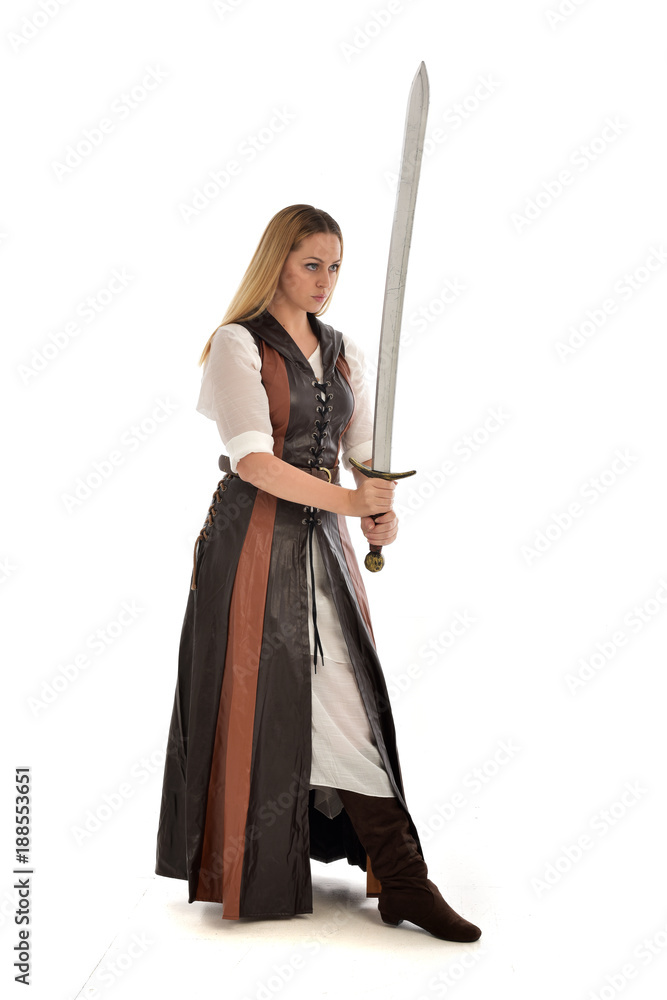 full length portrait of girl wearing brown  fantasy costume, holding a sword. standing pose on white studio background. 