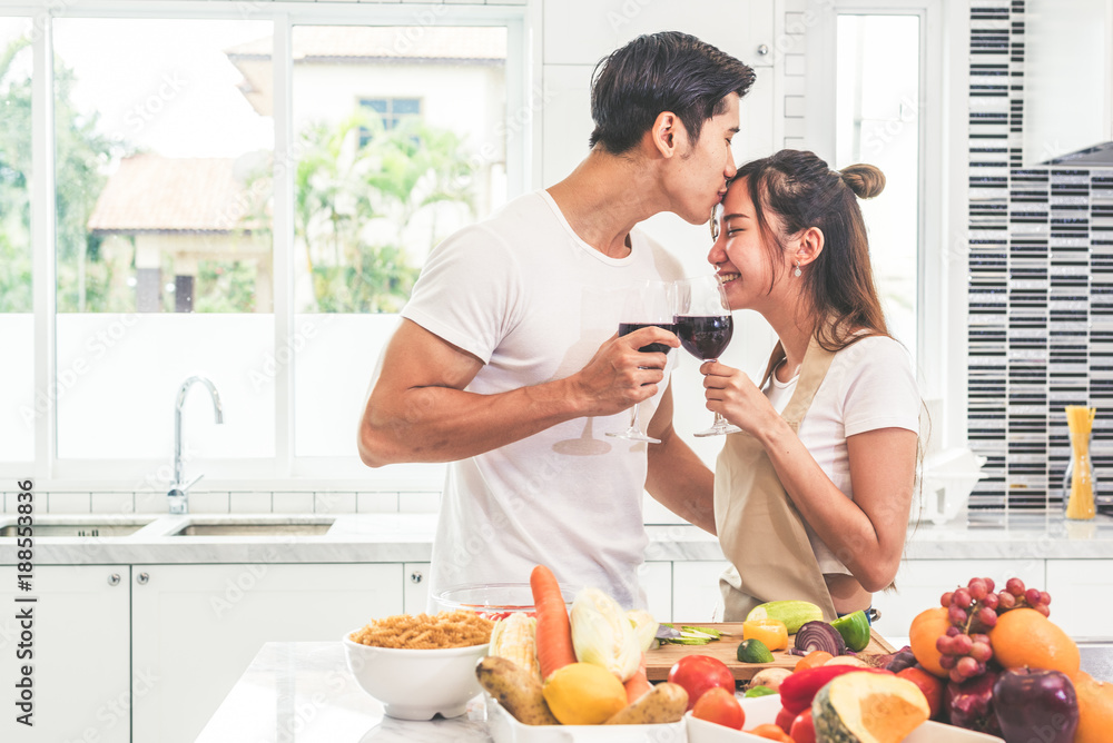 Asian lovers or couples kissing forehead and drinking wine in kitchen room at home. Love and happiness concept Sweet honeymoon and Valentine day theme