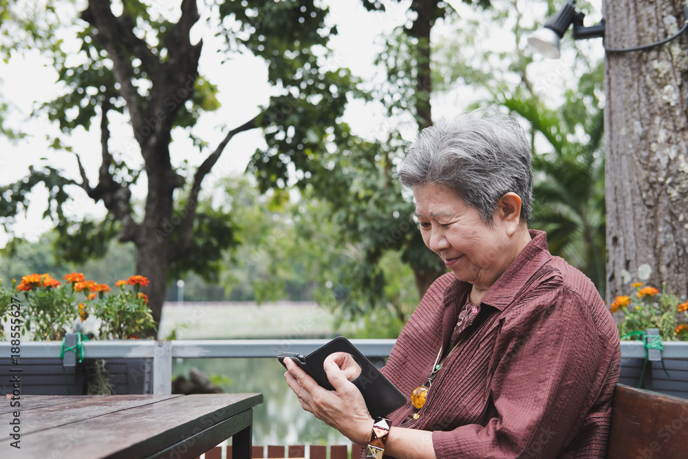 elder woman holding mobile phone in garden. elderly female texting message, using app with smartphone in park. senior use cellphone to connect with social network elder woman holding mobile phone in garden. elderly female texting message, using app with smartphone in park. senior use cellphone to connect with social network