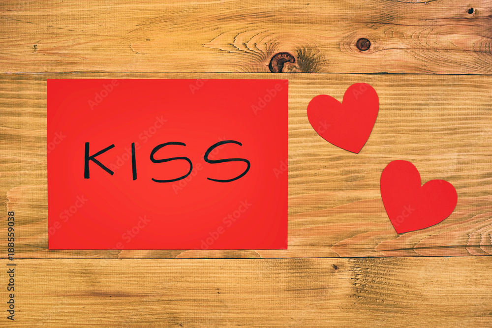 Red paper with word kiss and hearts on wooden table. Red paper with word kiss and hearts on wooden table.