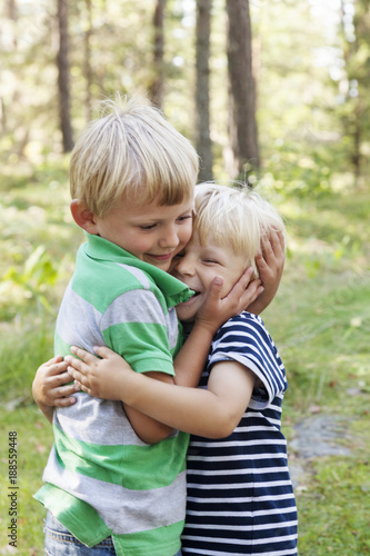 Two blonde boys hugging in forest