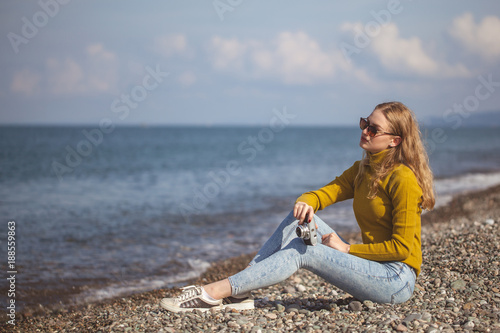 beautiful blonde girl on a sea beach with a old camera in hand