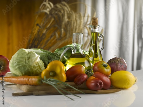 Fototapeta Naklejka Na Ścianę i Meble -  fresh vegetables and olive oil cruets on wooden cutting board and white marble kitchen table