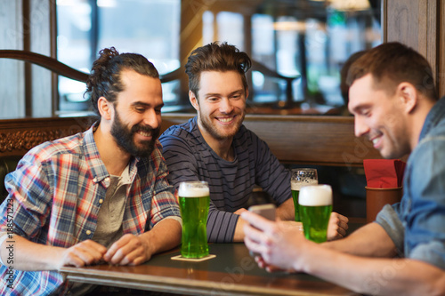 friends with smartphone drinking green beer at pub