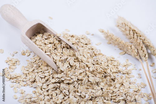 Oat flakes next to wooden spoon on white background. Isolated.