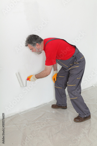 Adult worker painting wall to white with paint roller