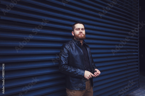 Outdoor portrait of handsome hipster man with beard in leather jacketon urban wall background.