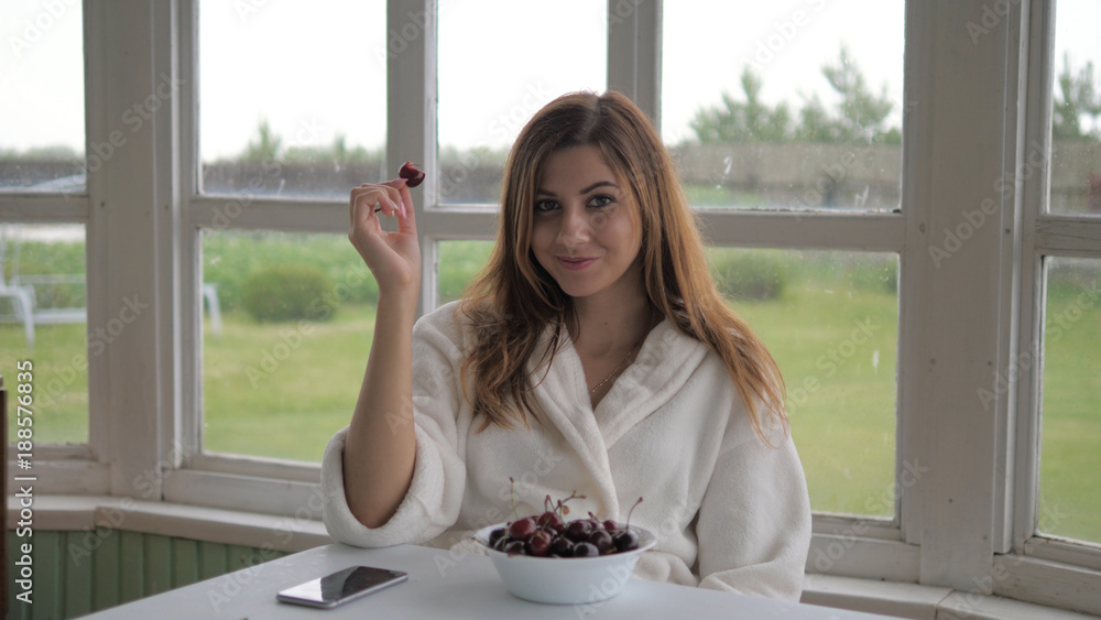 Cute girl in a white coat, sitting on the veranda and eating cherry. Cute girl in a white coat, sitting on the veranda and eating cherry.