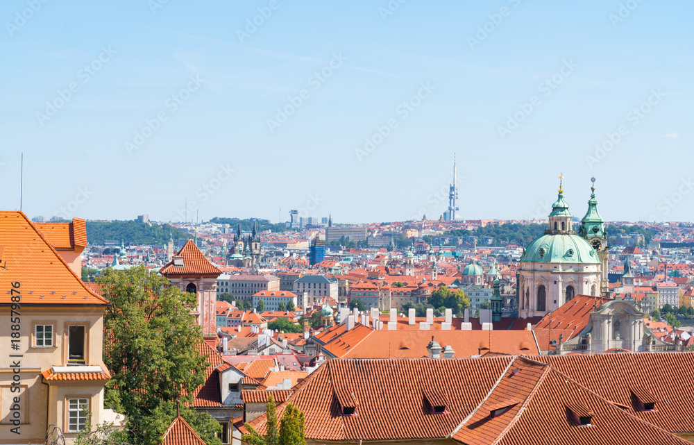 Obraz premium View across orange rooftops of Prague and city buildings under blue sky.