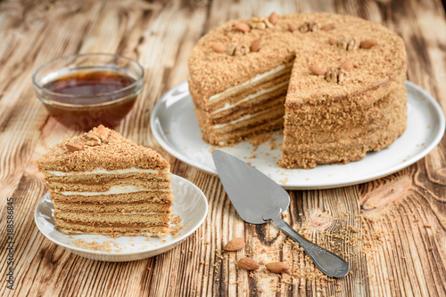 Код стоковой фотографии без лицензионных платежей — 781481086 Homemade layered honey cake with nuts and slice of cake on white plate on wooden table