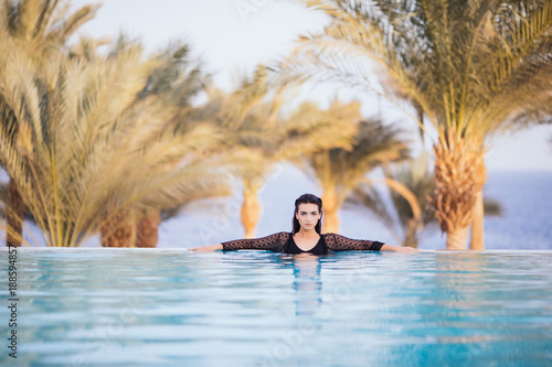 Fotografija girl in the infinity pool on the rooftop hotel relax in the water on sea and pal