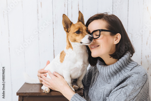 Photography Shot of attractive young woman embraces her favourite dog, touches with nose, expresses great love to pet
