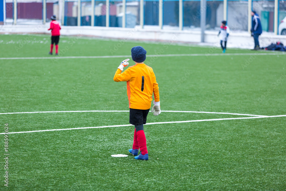 kid - goalkeeper plays football on the stadium at winter
