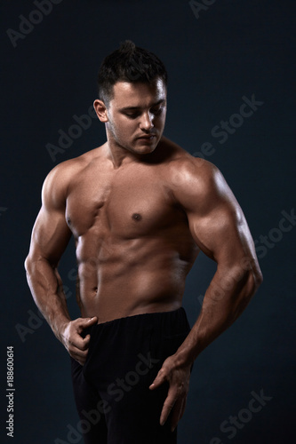 Muscular bodybuilder on black background.Strong athletic man shows body,abdominal muscles,chest muscles,biceps and triceps.Work out,gaining weight. Bodybuilding concept.