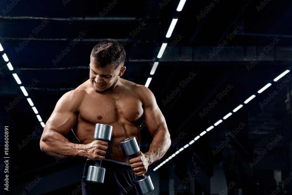 Muscular bodybuilder doing exercises with dumbbell in gym.Strong athletic man shows body,abdominal muscles,biceps and triceps.Work out,gaining weight,pumping up muscles with dumbbells. Muscular bodybuilder doing exercises with dumbbell in gym.Strong athletic man shows body,abdominal muscles,biceps and triceps.Work out,gaining weight,pumping up muscles with dumbbells.