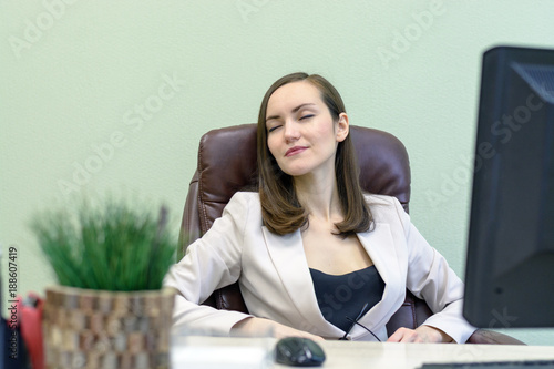 Female office worker sits in a leather chair in front of a computer and thinks