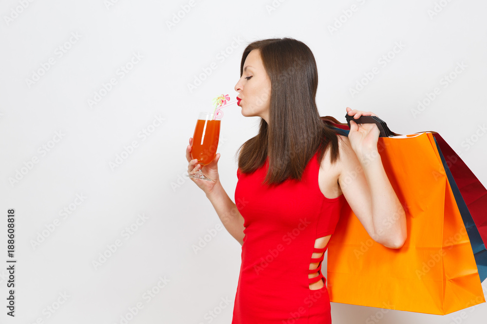 Attractive glamour fashionable young woman in red dress holding glass of drink cocktail, multi colored packets with purchases after shopping isolated on white background. Copy space for advertisement. Attractive glamour fashionable young woman in red dress holding glass of drink cocktail, multi colored packets with purchases after shopping isolated on white background. Copy space for advertisement.