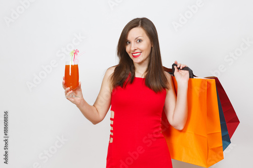 Attractive glamour fashionable young woman in red dress holding glass of drink cocktail, multi colored packets with purchases after shopping isolated on white background. Copy space for advertisement.