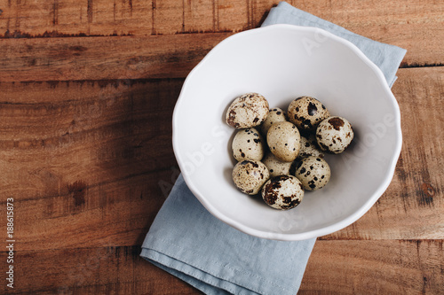 Quail eggs in white bowl, on wood table